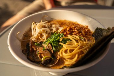 Vejetaryen ramen yakın plan. Mantarlı Asya eriştesi, nori ve yeşillik, güneş ışığında vegan yemeği, sokak restoranı, bulanık arka plan.