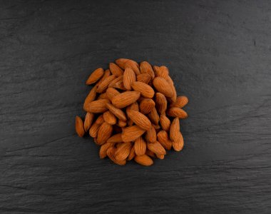 Badem yığını, fındık grubu, badem tohumları, kahverengi dağınık meyve çekirdekleri, siyah arka planda kuru çiğ fındık.