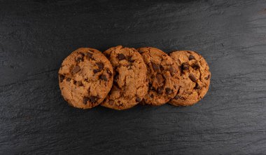 Çikolata parçalı kurabiyeler, Amerikan bisküvileri, kakaolu pasta, tatlı lokmalar fırın, siyah taştan arka planda yuvarlak pasta.