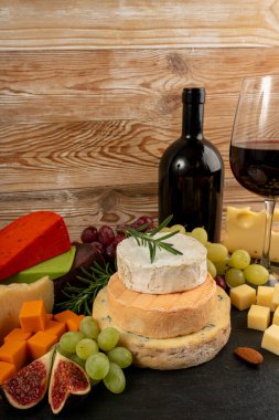 Peynir tabağı çeşitliliği, sarı, beyaz ve mavi gorgonzola tabağı kırmızı şarap bardağı, peynir tahtası, çeşitli doğranmış süt ürünleri, ahşap üzerinde kokulu Fransız peyniri.