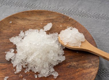 Ölü deniz tuzu yığını, vücut spası için beyaz kristaller, ezilmiş buza benzer sodyum klorür, ahşap tabakta spa fırçası.