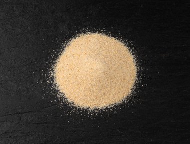 Sarımsak tozu, kurumuş granüle edilmiş ezilmiş sarımsak karanfilleri, küçük parçalara bölünmüş gıda malzemeleri, siyah arka planda baharat.