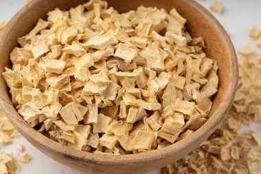 Kuru maydanoz kökü yığını, kurutulmuş kereviz küpleri, dağınık küçük meyan kökü parçaları, beyaz arka planda kuru sebze taneleri.