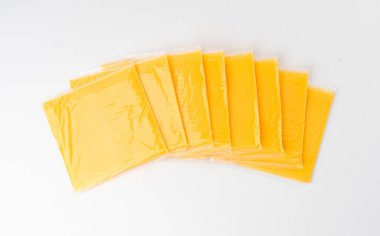 Amerikan peyniri izole edilmiş, işlenmiş peynir dilimi, ince sarı çedar peyniri, beyaz arka planda tost ve sandviç için plastik bir pakete sarılmış.