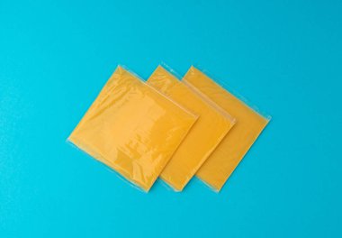 Amerikan peyniri, işlenmiş peynir dilimi, ince sarı çedar peyniri, kızarmış ekmek ve mavi arka planda sandviç paketi.