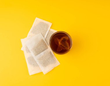 Bardakta bitki çayı kesesi, papatya çayı ve hiperikum ile sıcak su veya St. John 's Wort çay poşeti, tedavi amaçlı tıbbi içecek kupası, sarı arka planda çay poşeti demleme işlemi.