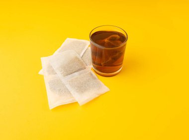 Bardakta bitki çayı kesesi, papatya çayı ve hiperikum ile sıcak su veya St. John 's Wort çay poşeti, tedavi amaçlı tıbbi içecek kupası, sarı arkaplanda çay poşeti demleme süreci.