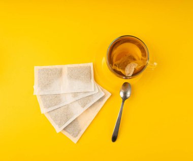 Fincanda bitki çayı kesesi, papatya çayı ve hiperikum ile sıcak su veya St. John 's Wort çay poşeti, tedavi amaçlı tıbbi içecek kupası, sarı arka planda çay poşeti demleme işlemi.