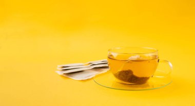 Fincanda bitki çayı kesesi, papatya çayı ve hiperikum ile sıcak su veya St. John 's Wort çay poşeti, tedavi amaçlı tıbbi içecek kupası, sarı arkaplanda çay poşeti demleme süreci.