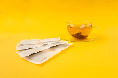 Fincanda bitki çayı kesesi, papatya çayı ve hiperikum ile sıcak su veya St. John 's Wort çay poşeti, tedavi amaçlı tıbbi içecek kupası, sarı arkaplanda çay poşeti demleme süreci.