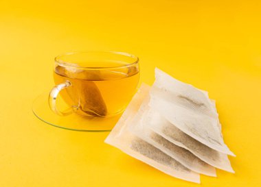 Fincanda bitki çayı kesesi, papatya çayı ve hiperikum ile sıcak su veya St. John 's Wort çay poşeti, tedavi amaçlı tıbbi içecek kupası, sarı arkaplanda çay poşeti demleme süreci.