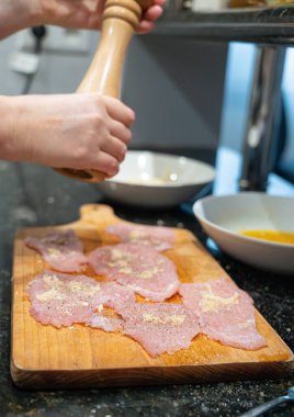 Şnitzel için yumuşatılmış et, ahşap biber değirmeni, hindi göğsü pişirme, ev yapımı şnitzel süreci.