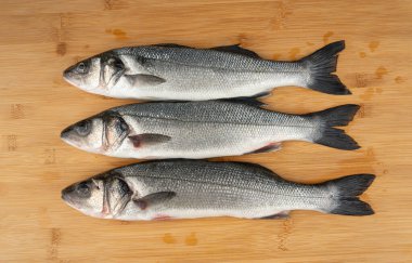 Avrupa deniz kabuğu veya Dicentrarchus labrax, tam çiğ labrax, taze deniz levreği, üç yaygın levrek balığı, beyaz baslar, beyaz kefal, deniz kestanesi, ahşap zemin üzerinde deniz ürünü.