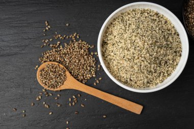 Kabuklu kenevir tohumları ahşap kasede, soyulmuş kenevir taneleri kaşıkta, kabuksuz marihuana çekirdekleri, siyah arka plan görünümlü yağ proteini kenevir tohumları yığını