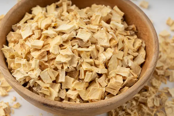 Kuru maydanoz kökü yığını, kurutulmuş kereviz küpleri, dağınık küçük meyan kökü parçaları, beyaz arka planda kuru sebze taneleri.