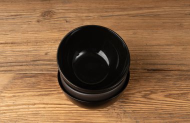 Masada boş kase yığını, ahşap masa üstünde siyah tabak, koyu porselen çanak modeli, metin üst görünümü için fotokopi alanı olan kırsal mutfak afişi.