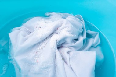 Çamaşırları mavi plastik bir leğende çamaşır deterjanı ve oksijen ağartıcı ile yıkamak, ıslak beyaz bez el yıkama.