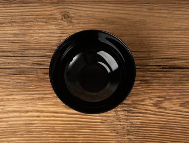 Masada boş kase, ahşap masa üstünde siyah tabak, siyah porselen çanak modeli, metin üst görünümü için fotokopi alanı olan kırsal mutfak pankartı.