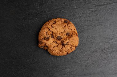 Çikolata parçalı kurabiyeler, Amerikan bisküvileri, kakaolu pasta, tatlı lokmalar fırın, siyah taştan arka planda yuvarlak pasta.