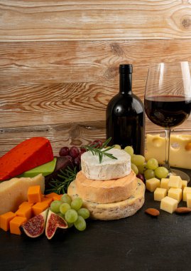Peynir tabağı çeşitliliği, sarı, beyaz ve mavi gorgonzola tabağı kırmızı şarap bardağı, peynir tahtası, çeşitli doğranmış süt ürünleri, ahşap üzerinde kokulu Fransız peyniri.
