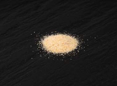 Sarımsak tozu, kurumuş granüle edilmiş ezilmiş sarımsak karanfilleri, küçük parçalara bölünmüş gıda malzemeleri, siyah arka planda baharat.