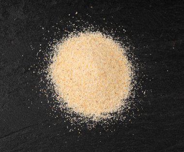 Sarımsak tozu, kurumuş granüle edilmiş ezilmiş sarımsak karanfilleri, küçük parçalara bölünmüş gıda malzemeleri, siyah arka planda baharat.