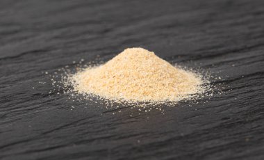 Sarımsak tozu, kurumuş granüle edilmiş ezilmiş sarımsak karanfilleri, küçük parçalara bölünmüş gıda malzemeleri, siyah arka planda baharat.