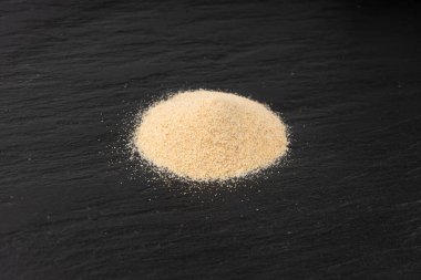 Sarımsak tozu, kurumuş granüle edilmiş ezilmiş sarımsak karanfilleri, küçük parçalara bölünmüş gıda malzemeleri, siyah arka planda baharat.