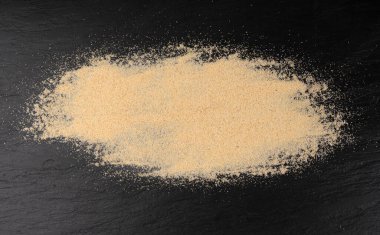 Sarımsak tozu, kurumuş granüle edilmiş ezilmiş sarımsak karanfilleri, küçük parçalara bölünmüş gıda malzemeleri, siyah arka planda baharat.