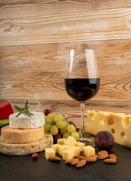 Peynir tabağı çeşitliliği, sarı, beyaz ve mavi gorgonzola tabağı kırmızı şarap bardağı, peynir tahtası, çeşitli doğranmış süt ürünleri, ahşap üzerinde kokulu Fransız peyniri.
