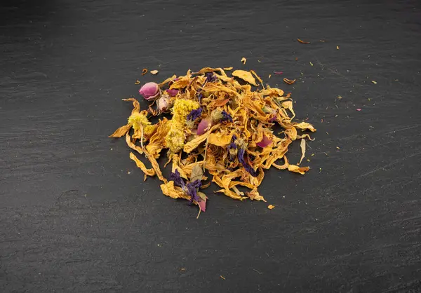 Kurutulmuş yenilebilir çiçek karışımı, Helichrysum arenaryum yığını, cüce yaprakları, siyah arka planda tıbbi bitki çayı yığını.