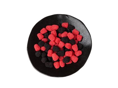 Siyah tabakta sakızlı meyveler, çiğnenmiş ahududular, jöle böğürtlenleri, kırmızı jelatin şekerler ve beyaz arka planda şeker tanecikleriyle kaplı siyah meyve meyveleri.