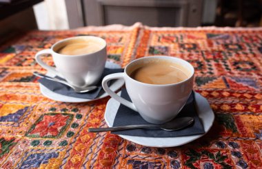 Beyaz bardakta sütlü çay, iki kupa, antika bir tekstil masa örtüsü olan bir masada birkaç fincan bulanık arka planda, seçici bir odak noktası olan retro tarzı bir restoranda.