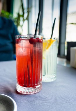 Lokanta masasında soğuk yaban mersini içeceği. Buzlu inek çileği çayı, kızılcık kokteyli ya da böğürtlen mors. Kırmızı böğürtlen suyu, meyve ezmesi, kırmızı içki, beyaz arka planda yaban mersini suyu, buz küpleri.