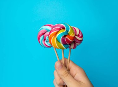 Elinde renkli lolipop, çubukta sarmal şeker, renkli çizgili lolipop, yuvarlak meyve şekeri, çok renkli şekerleme, mavi arka planda daire şeklinde lolipop, metin için kopyalama alanı