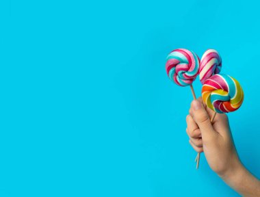 Elinde renkli lolipop, çubukta sarmal şeker, renkli çizgili lolipop, yuvarlak meyve şekeri, çok renkli şekerleme, mavi arka planda daire şeklinde lolipop, metin için kopyalama alanı