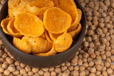 Humus nohut cipsleri yakın plan, cips yığını, makro portakal çerezi, kızarmış organik bakla gevreği, bulanık arka planda siyah kasede garbanzo fasulyesi atıştırmalıkları.