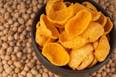 Humus nohut cipsleri yakın plan, cips yığını, makro portakal çerezi, kızarmış organik bakla gevreği, bulanık arka planda siyah kasede garbanzo fasulyesi atıştırmalıkları.