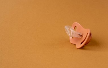 Emzik izole edilmiş, ortodontik bebek mankeni, lastik pastel çocuk yatıştırıcısı, kahverengi arka planda yeni sağlıklı silikon emzik.