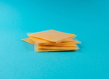 Amerikan peyniri, işlenmiş peynir dilimi, ince sarı çedar peyniri, kızarmış ekmek ve mavi arka planda sandviç paketi.