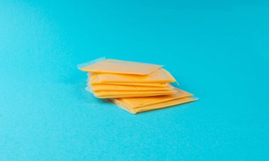 Amerikan peyniri, işlenmiş peynir dilimi, ince sarı çedar peyniri, kızarmış ekmek ve mavi arka planda sandviç paketi.