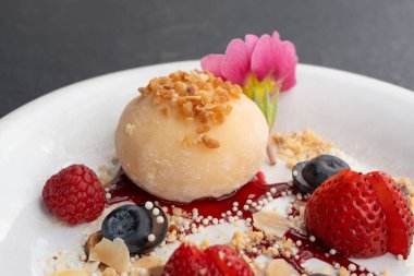 Meyveli mochi pirinç keki, beyaz daifuku, Japon geleneksel tatlısı, kremalı ve anko dolgulu yuvarlak wagashi, çilekli Asya şekeri, yaban mersini ve siyah arka planda çiçek.