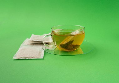 Fincanda bitki çayı kesesi, papatya çayı ve hiperikum ile sıcak su veya St. John 's Wort çay poşeti, tedavi amaçlı tıbbi içecek kupası, yeşil arka planda çay poşeti demleme süreci.