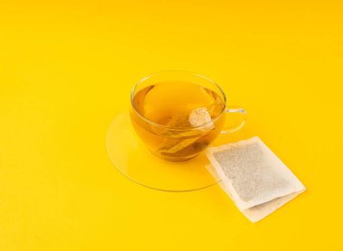 Fincanda bitki çayı kesesi, papatya çayı ve hiperikum ile sıcak su veya St. John 's Wort çay poşeti, tedavi amaçlı tıbbi içecek kupası, sarı arkaplanda çay poşeti demleme süreci.