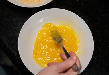 Kadın eli yumurtaları çatalla çırpar, ev yapımı şnitzel pişirme süreci, omlet hazırlama üst görünümü.