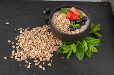 Siyah kasede pişirilmiş. Muzlu yulaf ezmesi sütlü yulaf lapası, çilek ve yabanmersini haşlanmış emmer, sağlıklı tahıl gevreği. Koyu arkaplanda taze yeşil naneli buğday taneleri.