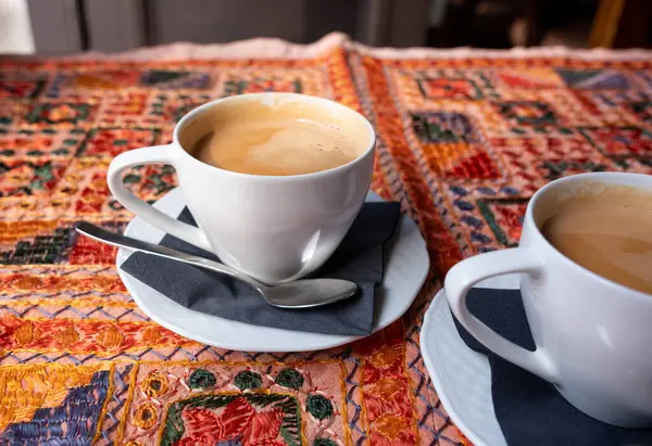 Beyaz bardakta sütlü çay, iki kupa, antika bir tekstil masa örtüsü olan bir masada birkaç fincan bulanık arka planda, seçici bir odak noktası olan retro tarzı bir restoranda.