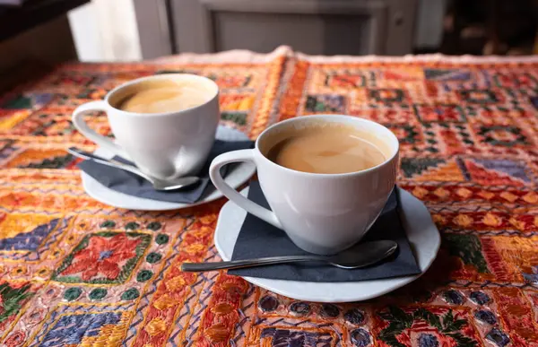 Beyaz bardakta sütlü çay, iki kupa, antika bir tekstil masa örtüsü olan bir masada birkaç fincan bulanık arka planda, seçici bir odak noktası olan retro tarzı bir restoranda.
