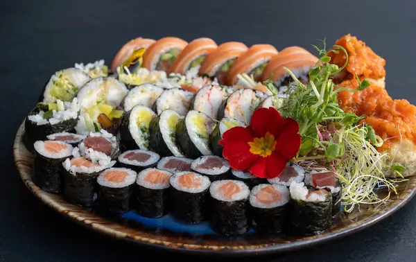 Somon, ton balığı, salatalık, avokado, yosun, pirinç, tempura sosu, mikroyeşillikler ve yenilebilir çiçeklerle çeşitli börekler. Japon yemek sunumunu seramik tabakta kapat