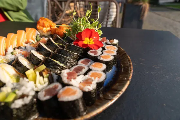 Somon, ton balığı, salatalık, avokado, yosun, pirinç, tempura sosu, mikroyeşillikler ve yenilebilir çiçeklerle çeşitli börekler. Japon yemek sunumunu seramik tabakta kapat
